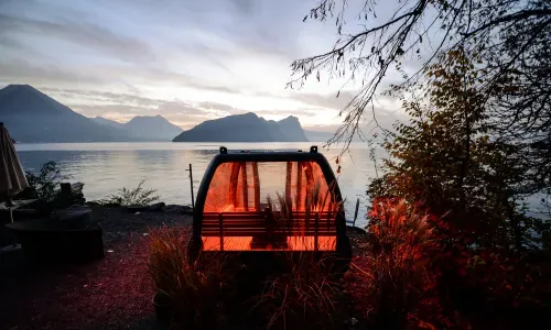 the glowing gondola sauna on the shore of lake lucerne at dusk, mountains behind